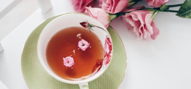 Tea cup with tea inside and pink flowers lying beside 