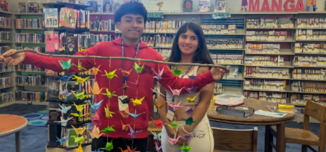 Two teens holding a stick with paper cranes