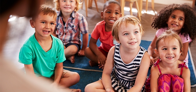Young children sitting on the floor of a library looking up. 