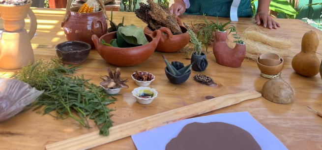 Different shaped clay jars holding corn, jicama and other plants sitting on top of a table. A flattened piece of clay is to the side.