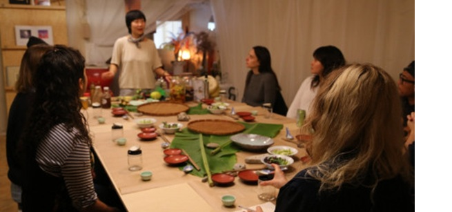 Picture of Jessica Wang giving a food preparation demo to people seated around a table.