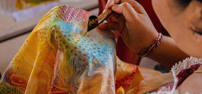 A woman hand painting a colorful piece of fabric, Image by AnglesNViews from Pixabay