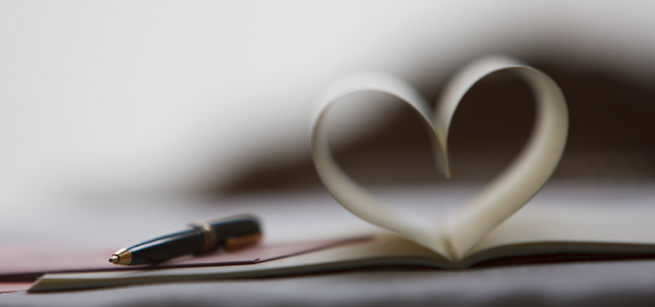 A black pen rests on an open book with pages folded to resemble a heart shape.