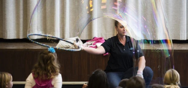 A Bubblologist makes a huge bubble in front of children.