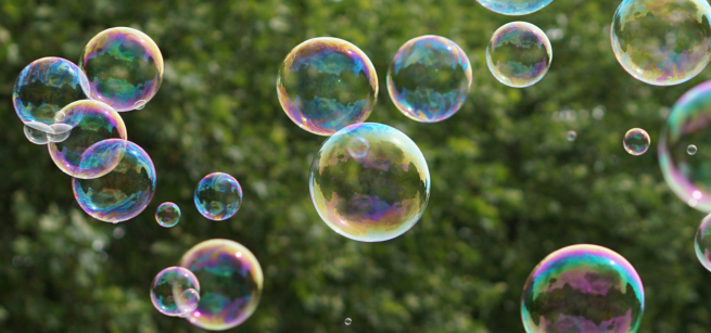 bubbles floating through the air in front of greenery