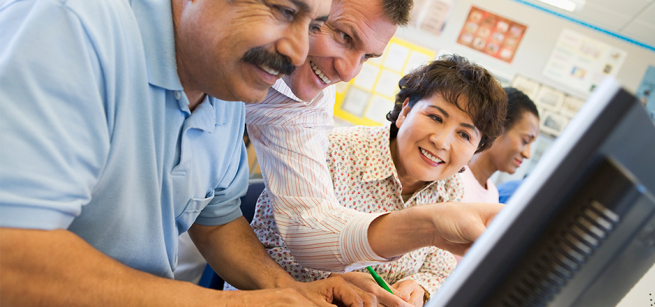 a man helps another man on a computer while a woman looks on