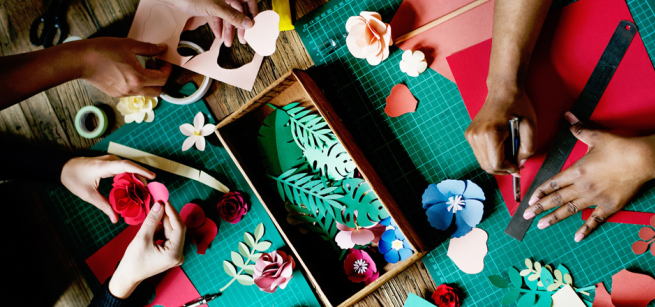 Three pairs of hands use crafting tools to make paper flowers.