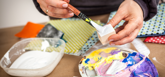 A table with paint supplies and a pair of hands painting a small block of wood.