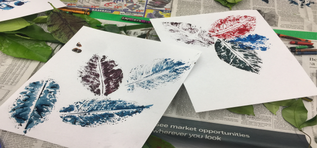 Pieces of paper with colorful images of leaves, actual leaves, and crayons, on top of pieces of newspaper