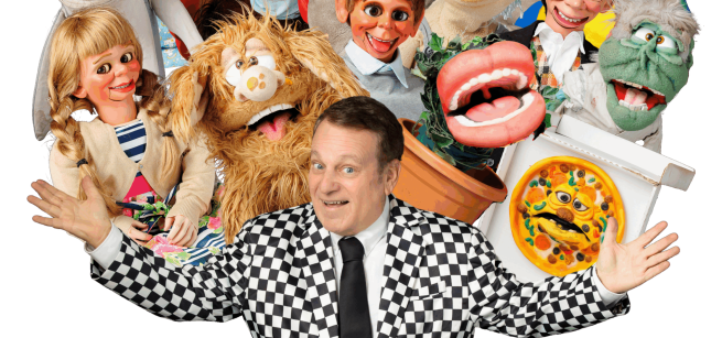 Smiling puppeter is surrounded by various puppets.