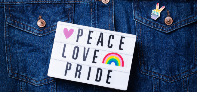 A jean jacket with a peace pride button on its pocket and a sign that says "peace, love, pride."