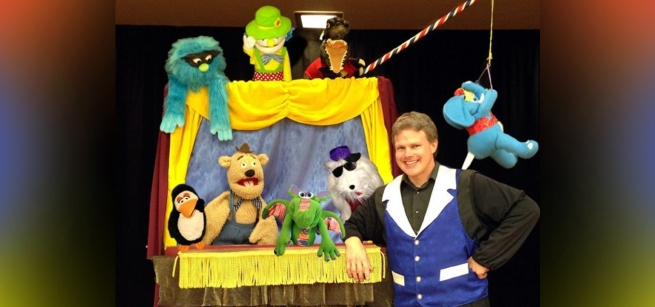 A man stands in front of a stage filled with different colored puppets.