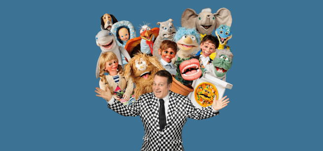 Ventriloquist Joe Gandelman in a white and black checkered suit with all of his puppets above his arms