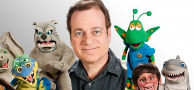 A smiling man is surrounded by colorful puppets