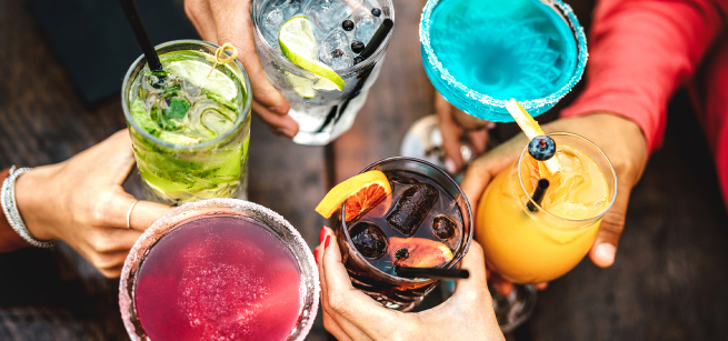 A group of people hold brightly colored drinks together