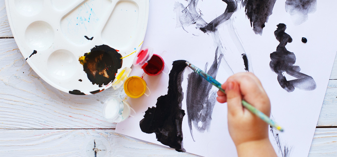 a young child's hand is using a brush to paint with black paint