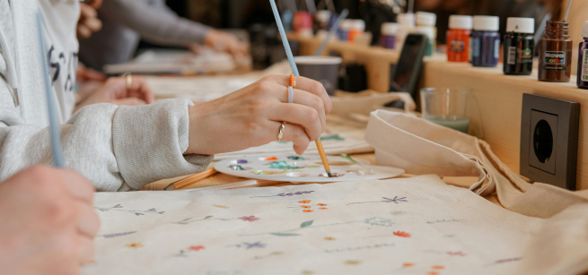 a woman is painting on a tote bag