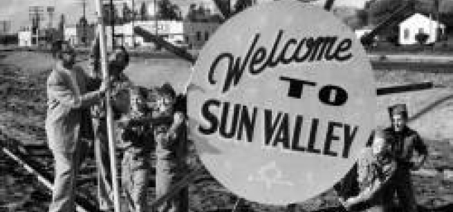 black and white photo of people around sign that reads welcome to sun valley