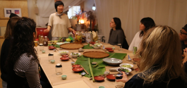 Chef Jess Wang teaching a cooking class to a table full of patrons. 
