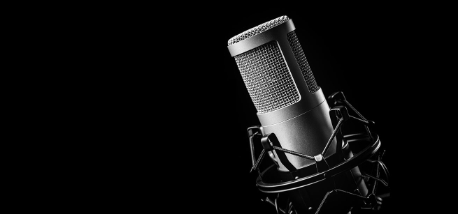A closeup of a podcasting microphone against a black background.