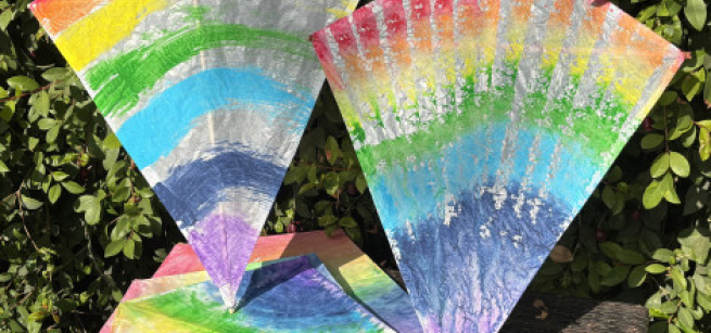 A pile of rainbow-painted kites against a leafy background.