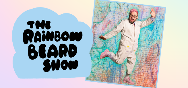 A photo of Ricky Rainbow Beard, with pink hair, a jumpsuit, and pink shoes, dancing in front of a colorful background that looks like crayon scribbles