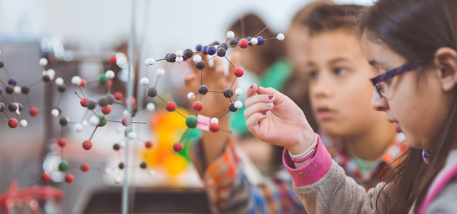 Several children are looking at a 3D model of atoms. 