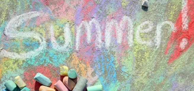 Colorful sidewalk chalk art with the word “Summer!” written on pavement beside scattered chalk pieces.