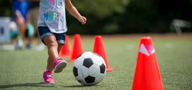 A child kicking a soccer ball between orange cones