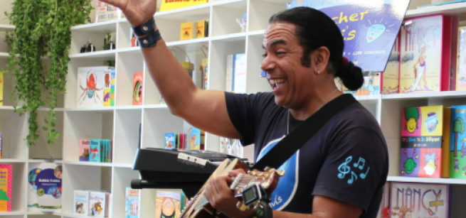 Teacher Davis with a guitar singing to an audience with a smile on his face