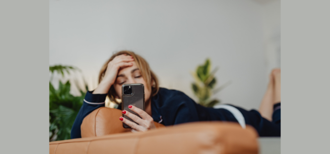 young person laying on a couch with a smartphone obscuring their face