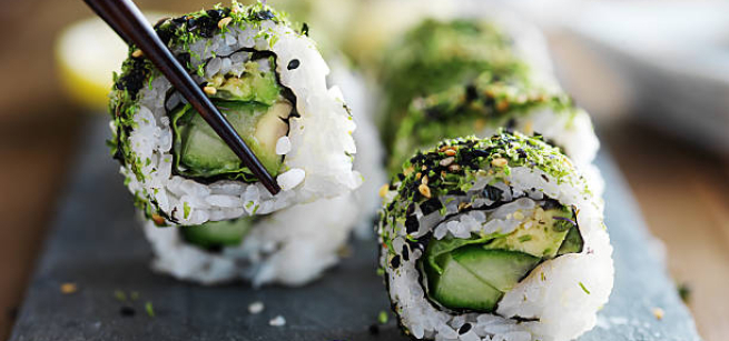 Multiple pieces of sushi with avocado on a black slab board 