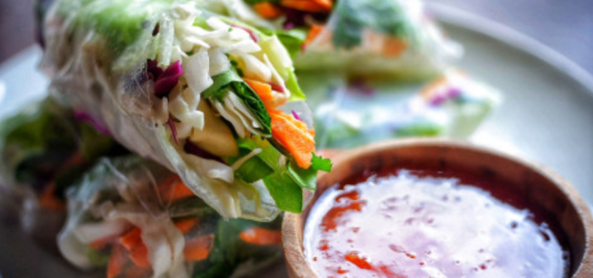 Fresh vegetable spring rolls filled with cabbage, carrots, and greens on a plate, served with a bowl of sweet chili sauce, creating a vibrant, appetizing scene.
