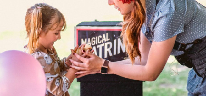 Little girl in a dress holding a bunny in front of the magician Katrina