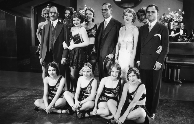 On the set of "The Woman Racket" at Metro-Goldwyn-Mayer Studios, Sir Jagjit Singh of India (in the center with moustache) is surrounded by a group of young starlets and chorus girls. 1930 – Eyre Powell Chamber of Commerce Collection
