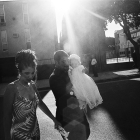 Black and white photo of woman holding hands with man, carrying baby dressed in white dress