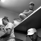 Black and white photo of two cell-mates on bunk beds and one making instant coffee