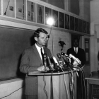 Man standing in front of a podium that has several microphones on top of it.