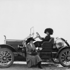 Women Drove Automobile Innovation, circa 1910, from the Security Pacific National Bank Collection. The photo features two women, one sitting in the driver's seat, the other sitting on a ledge on the outside of the car.