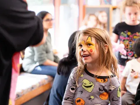 A young girl with her face painted smiles in a group of other children.