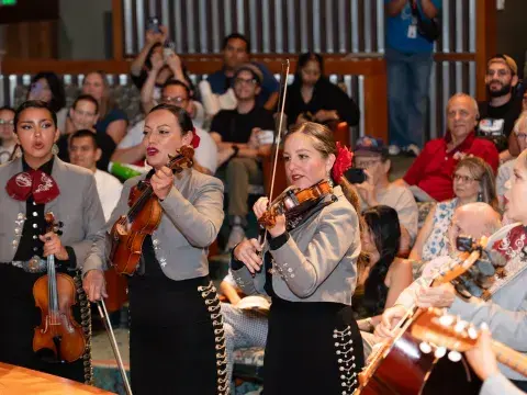 Four musicians in matching uniforms play stringed instruments in the midst of an audience.