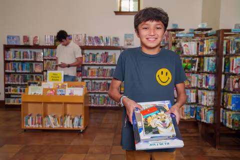Kid holds stack of books at the library