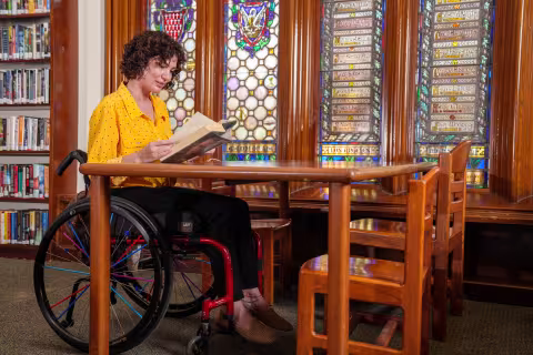 adult in wheelchair reads book at library table