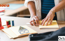 image of two hands folding a zine on a table with threads and art materials.