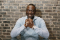 Yusef Salaam with hands clasped leaning against a brick wall