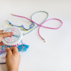 hands hold a foam kumihimo disk and there are braids demonstrating the technique