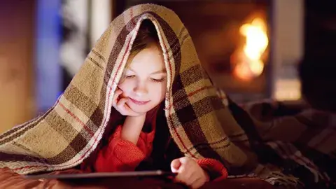 Young girl reading under a warm blanket