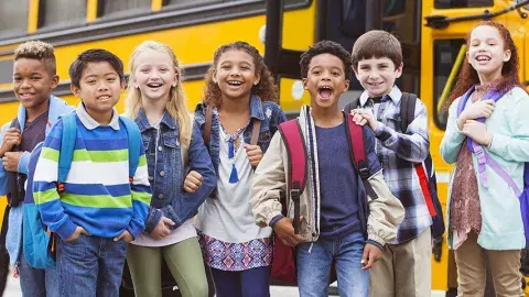 Happy, laughing diverse tweens standing near a school bus