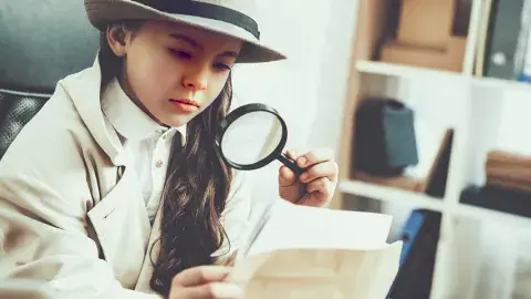 Young girl investigating photos with magnifying glass.