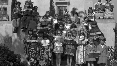 Children dressed in the costumes of many different countries hold signs indicating the languages in which books are available at the Los Angeles Public Library, ca 1939 